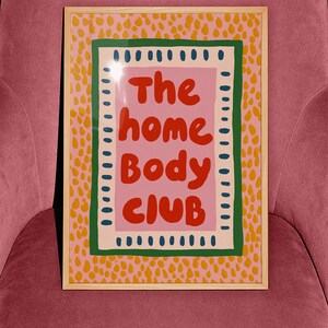 Playful typography poster featuring the phrase The Home Body Club in bold red lettering on a soft pink background. Framed with green and cream borders and surrounded by mustard yellow abstract dots, this colorful maximalist design blends cozy lifestyle humor with eclectic pattern layering and retro-inspired charm.Home Body Poster, Typography Wall Art, Cozy Quote Print, Maximalist Decor, Eclectic Print, Retro Style Poster, Entryway Wall Decor, Bold Letter Art, Trendy Art Print, Dopamine Color Art