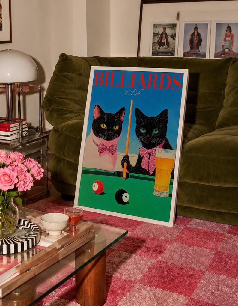 Funny cats playing pool poster featuring two black-faced cats wearing pink patterned bows behind a bright green billiards table. One tuxedo cat has a white body and yellow eyes, while the other is black with green eyes and holds an orange pool cue. Red and black billiard balls marked 8 and 7 sit on the felt beside a glass of golden beer. Large red BILLIARDS lettering, delicate Club script stand out against a vivid blue background. This quirky cat artwork suits game room, home bar, gallery wall.