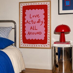 A playful pink and red typography print featuring the hand-lettered message “Love Actually All Around” inside a scalloped frame. The warm peach background, bold lettering and imperfect drawn texture give the artwork a cheerful, handmade character. Designed for bedrooms, living rooms, gallery walls or an above-bed display, this romantic wall art adds color without feeling overly formal. A thoughtful choice for anniversaries, Valentine’s Day, newlyweds or anyone who loves expressive quote posters.