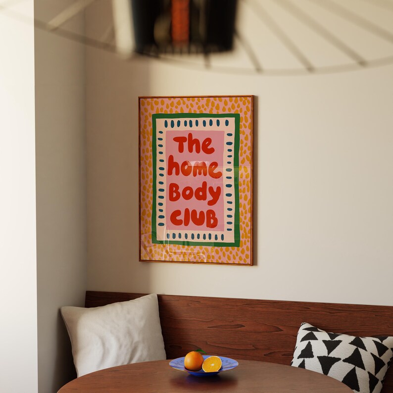 Playful typography poster featuring the phrase The Home Body Club in bold red lettering on a soft pink background. Framed with green and cream borders and surrounded by mustard yellow abstract dots, this colorful maximalist design blends cozy lifestyle humor with eclectic pattern layering and retro-inspired charm.Home Body Poster, Typography Wall Art, Cozy Quote Print, Maximalist Decor, Eclectic Print, Retro Style Poster, Entryway Wall Decor, Bold Letter Art, Trendy Art Print, Dopamine Color Art