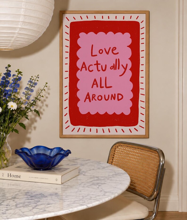 A playful pink and red typography print featuring the hand-lettered message “Love Actually All Around” inside a scalloped frame. The warm peach background, bold lettering and imperfect drawn texture give the artwork a cheerful, handmade character. Designed for bedrooms, living rooms, gallery walls or an above-bed display, this romantic wall art adds color without feeling overly formal. A thoughtful choice for anniversaries, Valentine’s Day, newlyweds or anyone who loves expressive quote posters.