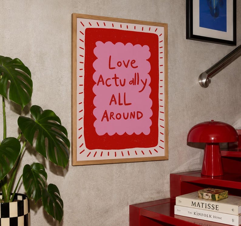 A playful pink and red typography print featuring the hand-lettered message “Love Actually All Around” inside a scalloped frame. The warm peach background, bold lettering and imperfect drawn texture give the artwork a cheerful, handmade character. Designed for bedrooms, living rooms, gallery walls or an above-bed display, this romantic wall art adds color without feeling overly formal. A thoughtful choice for anniversaries, Valentine’s Day, newlyweds or anyone who loves expressive quote posters.