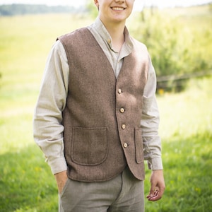 Op de afbeelding: Een bruin tweed vest met twee voorzakken en houten knopen. Het vest wordt gedragen over een lichtgekleurd overhemd en gecombineerd met een grijze broek. Een bijpassende tweed pet maakt de outfit compleet, geschikt voor buitenactiviteiten.