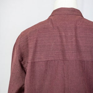 May include: A long-sleeved shirt in a deep burgundy color. The shirt is made of a textured fabric and has a simple, classic design.