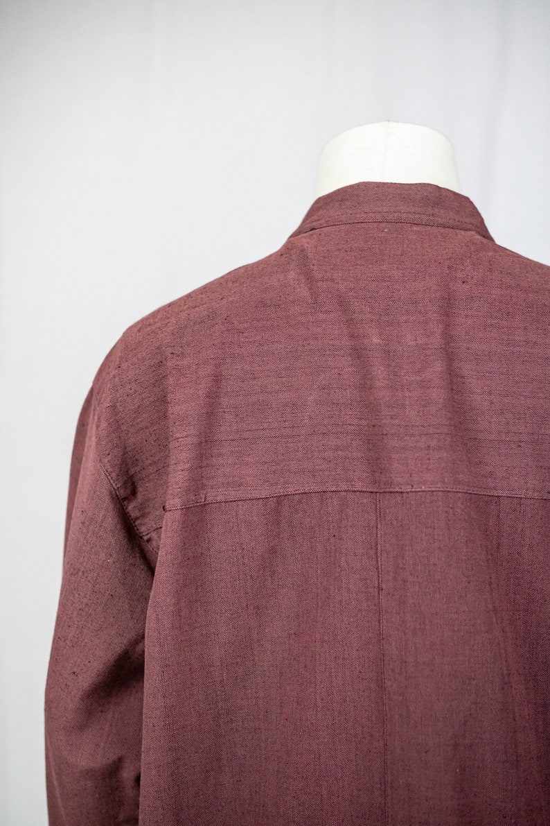 May include: A long-sleeved shirt in a deep burgundy color. The shirt is made of a textured fabric and has a simple, classic design.