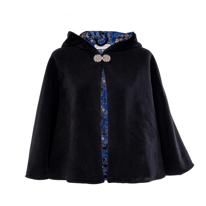 May include: A black hooded cape featuring a silver-toned circular clasp at the neckline. The interior lining is a vibrant blue fabric decorated with a detailed gold and white floral pattern. The garment is open at the front, revealing the lining.