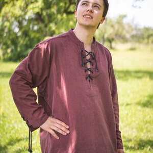 May include: A maroon long-sleeved shirt with a lace-up neckline. The shirt is made of a soft, comfortable fabric and has a relaxed fit.
