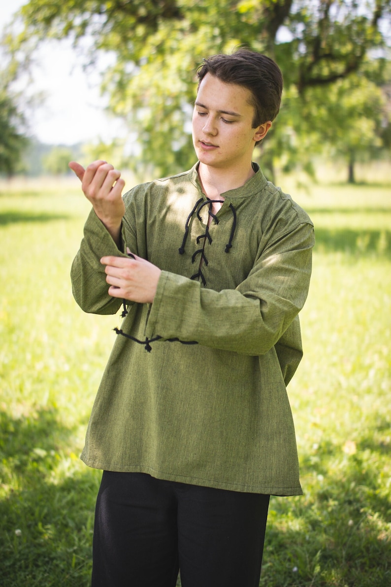 May include: A green long-sleeved shirt with a black lace-up detail at the neckline. The shirt is made of a soft, textured fabric.