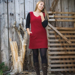 Puede incluir: Una mujer con un vestido rojo de punto con mangas negras y medias negras. Est&aacute; de pie frente a una pared de madera y una valla de madera. Lleva botas marrones.