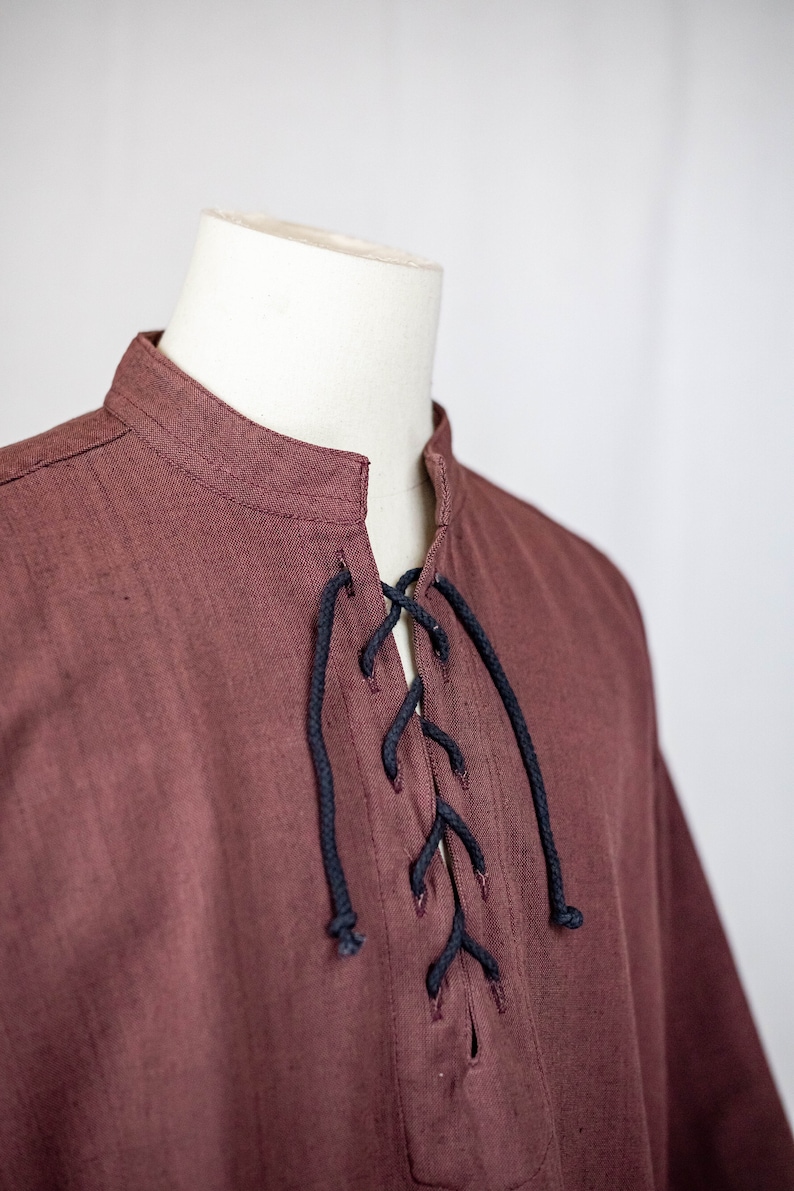 May include: A maroon shirt with a black lace-up neckline. The shirt has a mandarin collar and long sleeves.