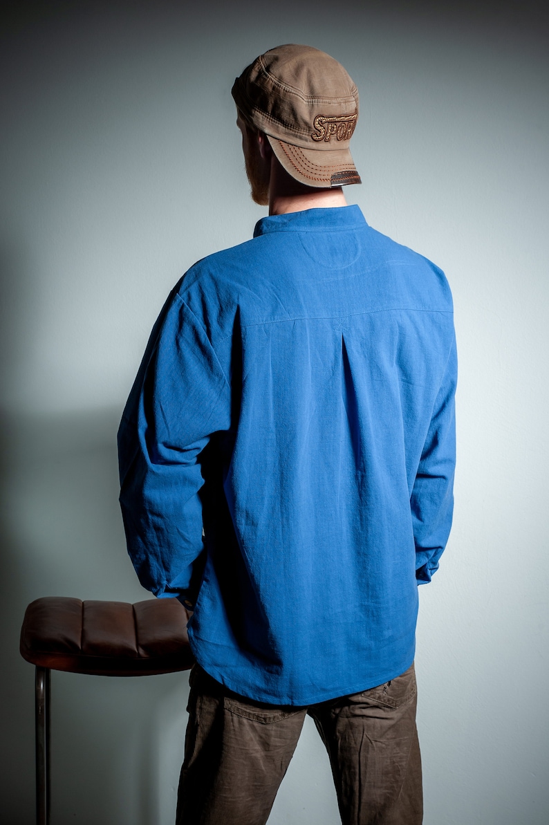 Op de afbeelding: Een persoon draagt een blauw lang mouw shirt met een bruine baseballpet met daarop "Sport". De persoon staat voor een lichtgrijze muur.