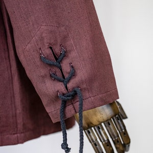 May include: A burgundy linen jacket with black lace-up detail on the sleeve cuffs.