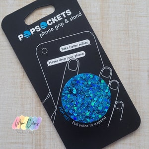 May include: A turquoise blue glitter PopSocket phone grip and stand. The packaging shows a phone with the PopSocket attached and the text "Take better selfies. Never drop your phone. Pop Me! Pull twice to expand."