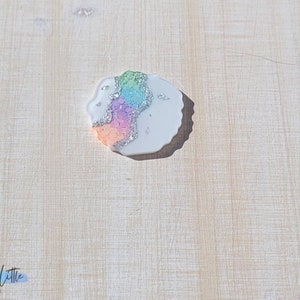 May include: A white resin cabochon with a rainbow agate design and silver glitter accents.