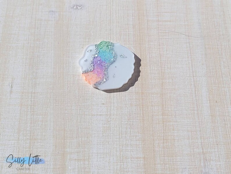 May include: A white resin cabochon with a rainbow agate design and silver glitter accents.