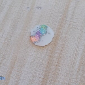 May include: A small, round, white, resin coaster with a rainbow glitter design.