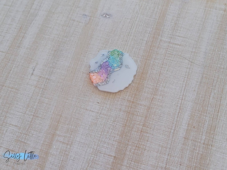 May include: A small, round, white, resin coaster with a rainbow glitter design.