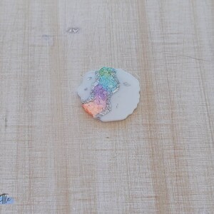 May include: A white resin coaster with a colorful agate design. The coaster has a rainbow of colors including pink, orange, yellow, green, and blue. The coaster is covered in silver glitter.
