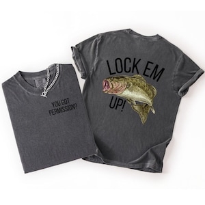 May include: Two charcoal gray t-shirts. One shirt has the text "YOU GOT PERMISSION?" and a silver chain. The other shirt has a graphic of a fish with the text "LOCK EM UP!"