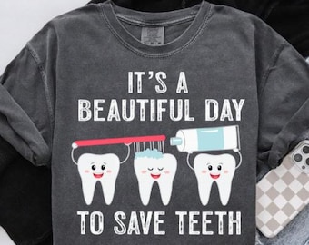 Op de afbeelding: Donkergrijze sweatshirt met de tekst "IT'S A BEAUTIFUL DAY TO SAVE TEETH". De afbeelding toont drie lachende tanden, een tandenborstel en een tube tandpasta. De sweatshirt heeft een ronde hals.