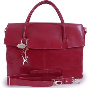 May include: A deep red leather handbag featuring a top handle and a detachable shoulder strap. A silver-toned chain charm hangs from the handle, displaying a small oval tag with the text CATWALK and a stylised silver cat figure with orange beads.