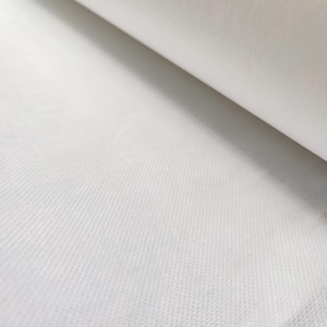 Peut inclure: Gros plan sur un tissu non tissé blanc avec un motif texturé subtil. Le tissu est enroulé, montrant la surface lisse du rouleau.