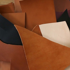 Puede incluir: Surtido de recortes de cuero en varios colores, incluyendo marrón, tostado, negro y crema. Las piezas de cuero están dispuestas en un patrón aleatorio, mostrando diferentes texturas y tonos.