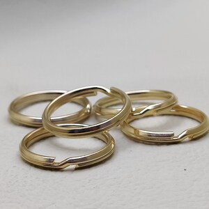 May include: Five gold-coloured metal key rings, stacked on top of each other.