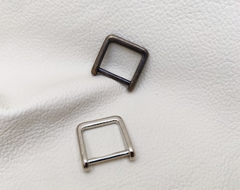 May include: Two metal D-rings, one silver and one antique brass, on a white background.