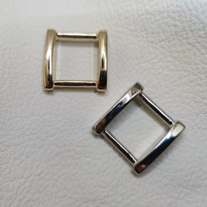 May include: Two metal D-rings, one gold and one silver, on a white background.