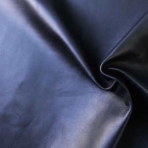 Op de afbeelding: Een close-up van een glad, donkerblauw lederen stof. De stof is gevouwen en gedrapeerd, waardoor de textuur en glans zichtbaar worden.