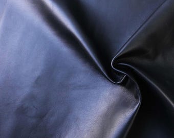 May include: A close-up of a smooth, dark blue leather fabric. The fabric is folded and draped, showing its texture and sheen.