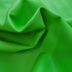 Peut inclure: Gros plan sur un tissu vert vif à la texture lisse et brillante. Le tissu est plié et drapé, créant des lignes douces et fluides.