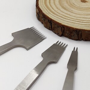 May include: Three leather stitching tools with metal handles and different sized stitching heads. The tools are on a white surface.