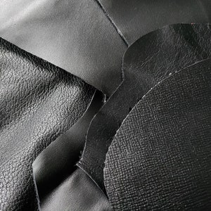 Könnte beinhalten: Nahaufnahme von schwarzem Leder mit verschiedenen Texturen. Das Leder hat eine glatte, genarbte und strukturierte Maserung.