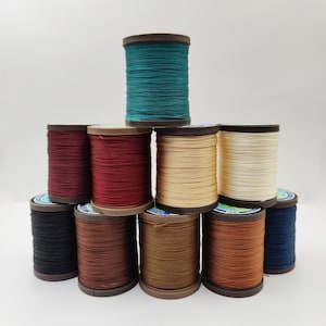 May include: A collection of ten spools of thread in various colours, including red, brown, beige, blue, and green. The spools are arranged in a pyramid shape.