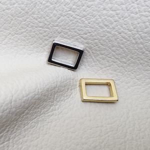 Könnte beinhalten: Zwei Metallrahmenformen, eine silberne und eine goldene, auf einem weißen strukturierten Hintergrund.