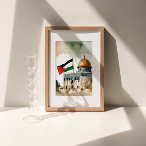 May include: A framed watercolor painting of the Dome of the Rock in Jerusalem, with a Palestinian flag waving in the wind. The painting is set against a light blue sky with white clouds.