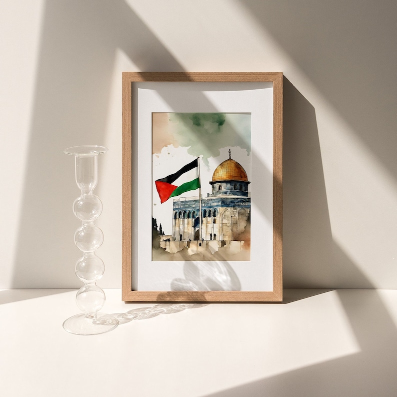 May include: A framed watercolor painting of the Dome of the Rock in Jerusalem, with a Palestinian flag waving in the wind. The painting is set against a light blue sky with white clouds.