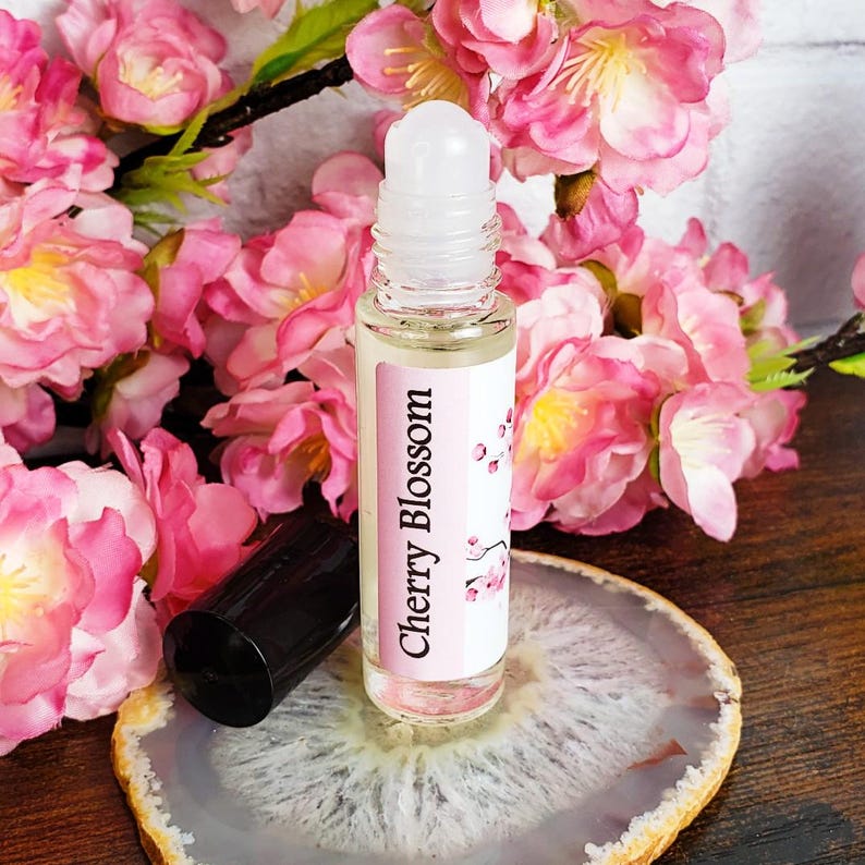 May include: A clear glass roller bottle with a white roller ball and a pink label that says "Cherry Blossom". The bottle is sitting on a white and gray agate slice.