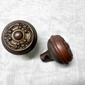 May include: Two antique door knobs with ornate designs. One is round with a raised center and the other is round with a raised edge.