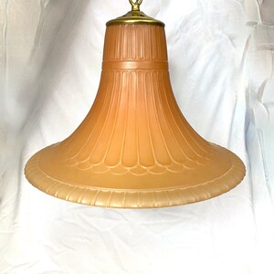 May include: A large, brown glass pendant light fixture with a decorative, ribbed design. The fixture has a brass chain and a brass cap.