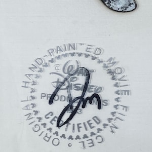 Pu&ograve; includere: Un celluloide di produzione Disney con una firma e un timbro che recita "Original Hand-Painted Movie Film Cel Certified". L'immagine include una scarpa e il logo Disney.