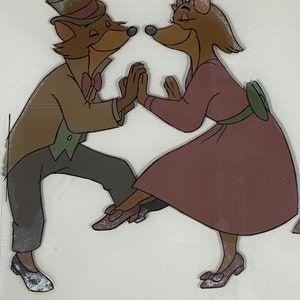 Pu&ograve; includere: Illustrazione animata di due volpi antropomorfe che ballano. La volpe maschio indossa un abito marrone, un cappello a cilindro e un papillon. La volpe femmina indossa un vestito malva con una cintura e un fiocco verdi. Si tengono per mano e sorridono.