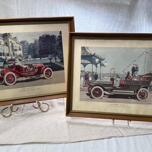 May include: Two framed vintage prints of antique cars. The top print shows a red 1909 Mercedes, a 'car of the modern age'. The bottom print shows a black 1907 Ford Model K, a 'car of the modern age'.