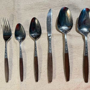 May include: Set of seven silver-toned flatware with brown wooden handles. The set includes two forks, two spoons, a butter knife, and two teaspoons.