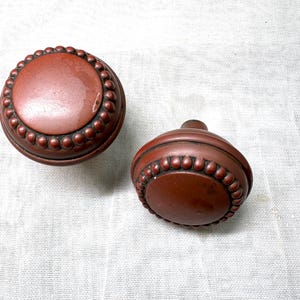 May include: Two round, brown door knobs with a beaded edge.