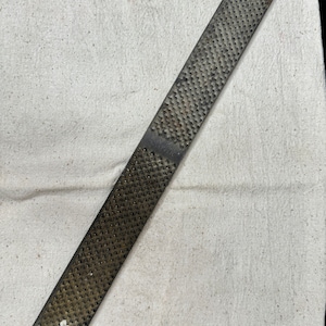 May include: A long, black metal rasp with a rough, textured surface. The rasp is approximately 12 inches long.