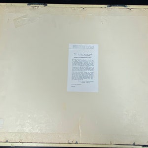 Pu&ograve; includere: Retro di una stampa incorniciata con sfondo color crema. La cornice &egrave; di colore beige chiaro. Un'etichetta bianca con testo &egrave; apposta sulla stampa. La stampa ha due ganci di metallo attaccati in alto.
