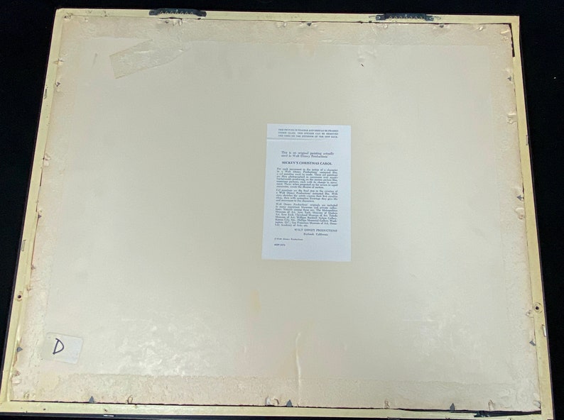 Pu&ograve; includere: Retro di una stampa incorniciata con sfondo color crema. La cornice &egrave; di colore beige chiaro. Un'etichetta bianca con testo &egrave; apposta sulla stampa. La stampa ha due ganci di metallo attaccati in alto.
